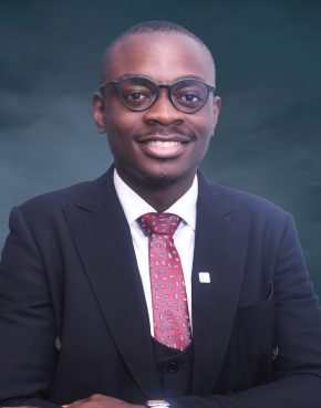 Bespectacled smiling African man in a dark suit, white shirt and floral tie.