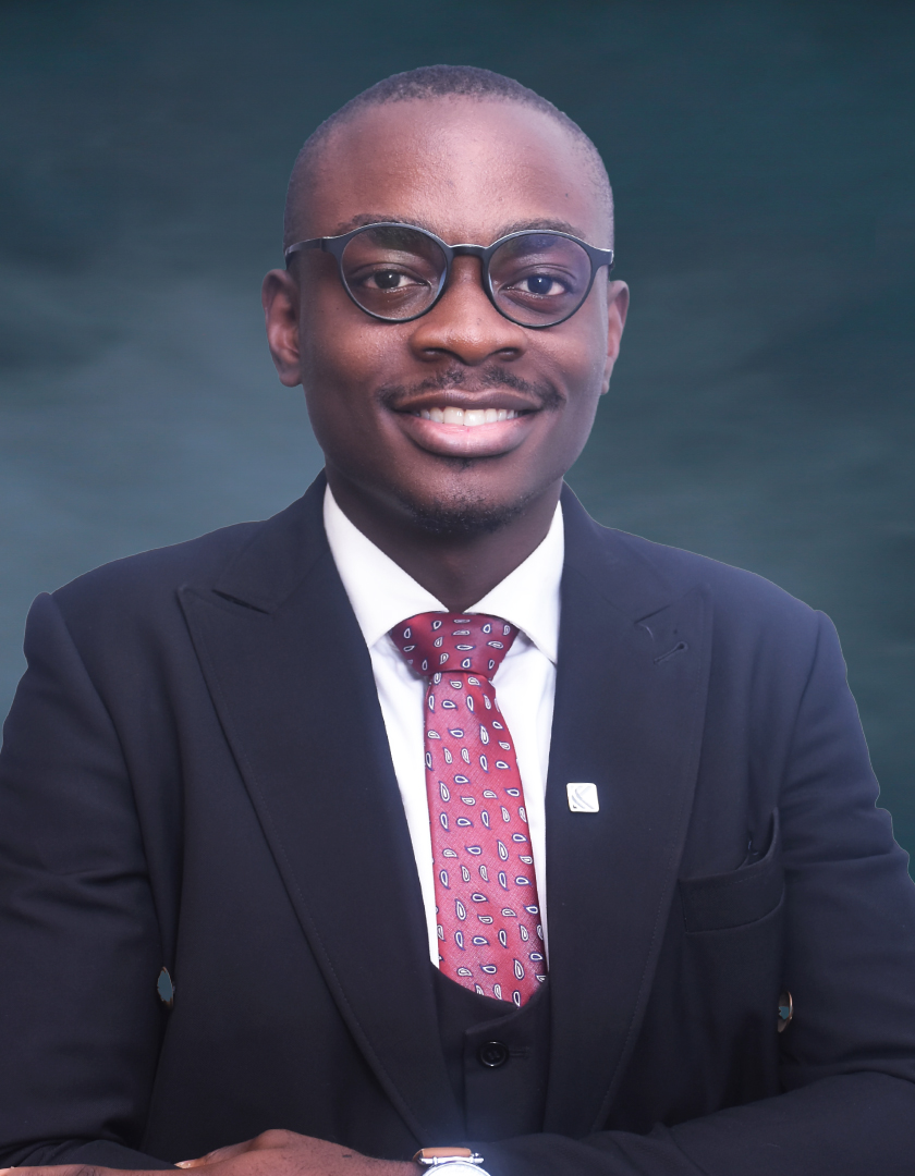 Bespectacled smiling African man in a dark suit, white shirt and floral tie.