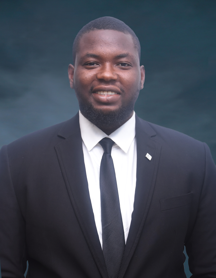 Smiling African man in a white shirt, black tie and black suit, complete with a lapel pin.