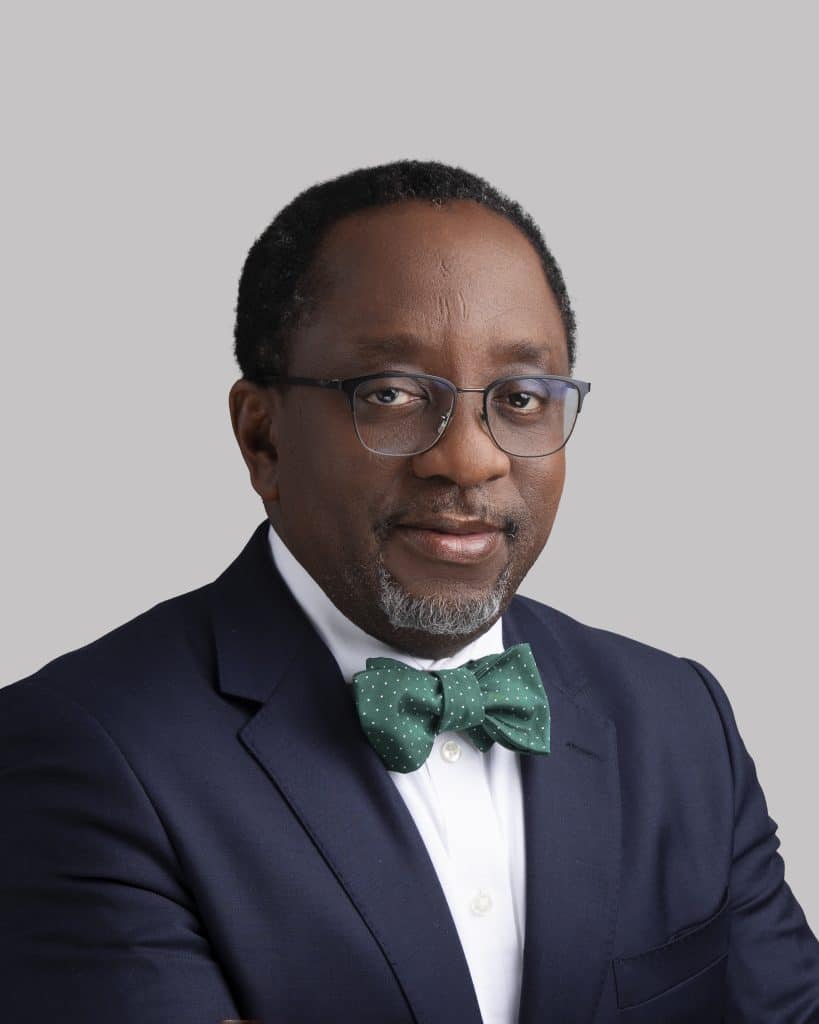 Darkskinned bespectacled man posing in a blue syit, white shirt and green bow tie