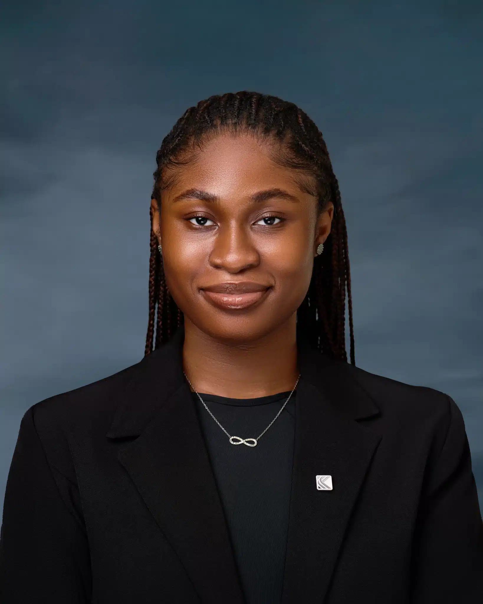 Brown-skinned African woman in long braids, black jacket, a lapel pin and necklace