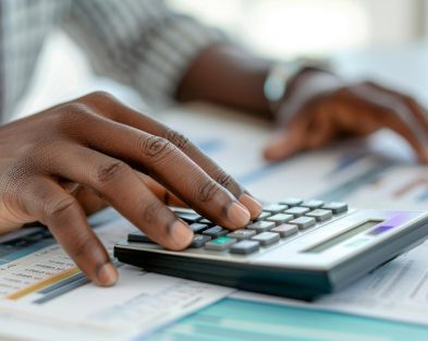 AI-generated image of the hands of a black man with rolled sleeves and wristwatch using a calculator on a table with spreadsheets