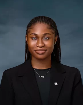 Brown-skinned African woman in long braids, black jacket, a lapel pin and necklace